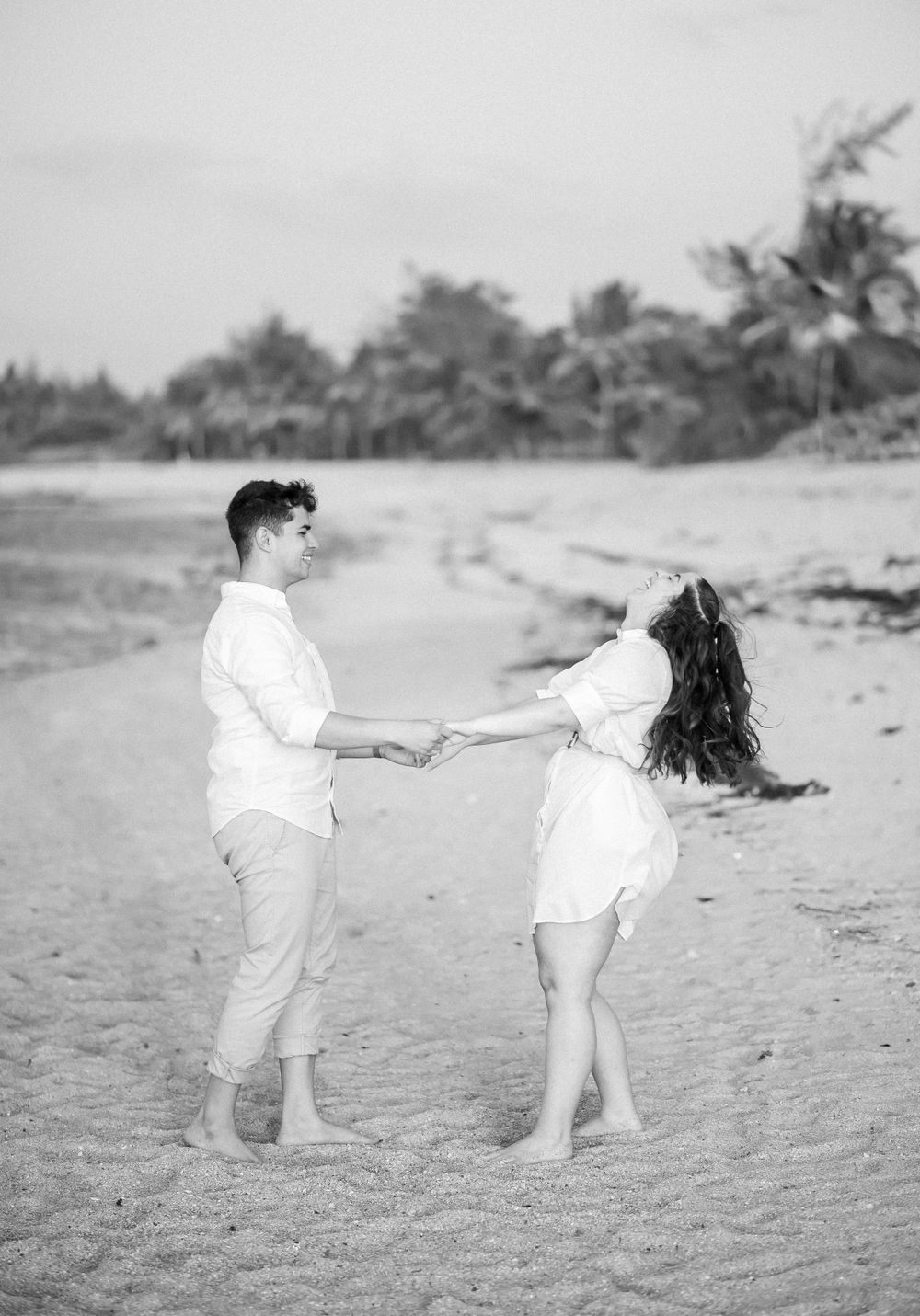 A couple in white clothing dancing and spinning on a palm-lined beach.