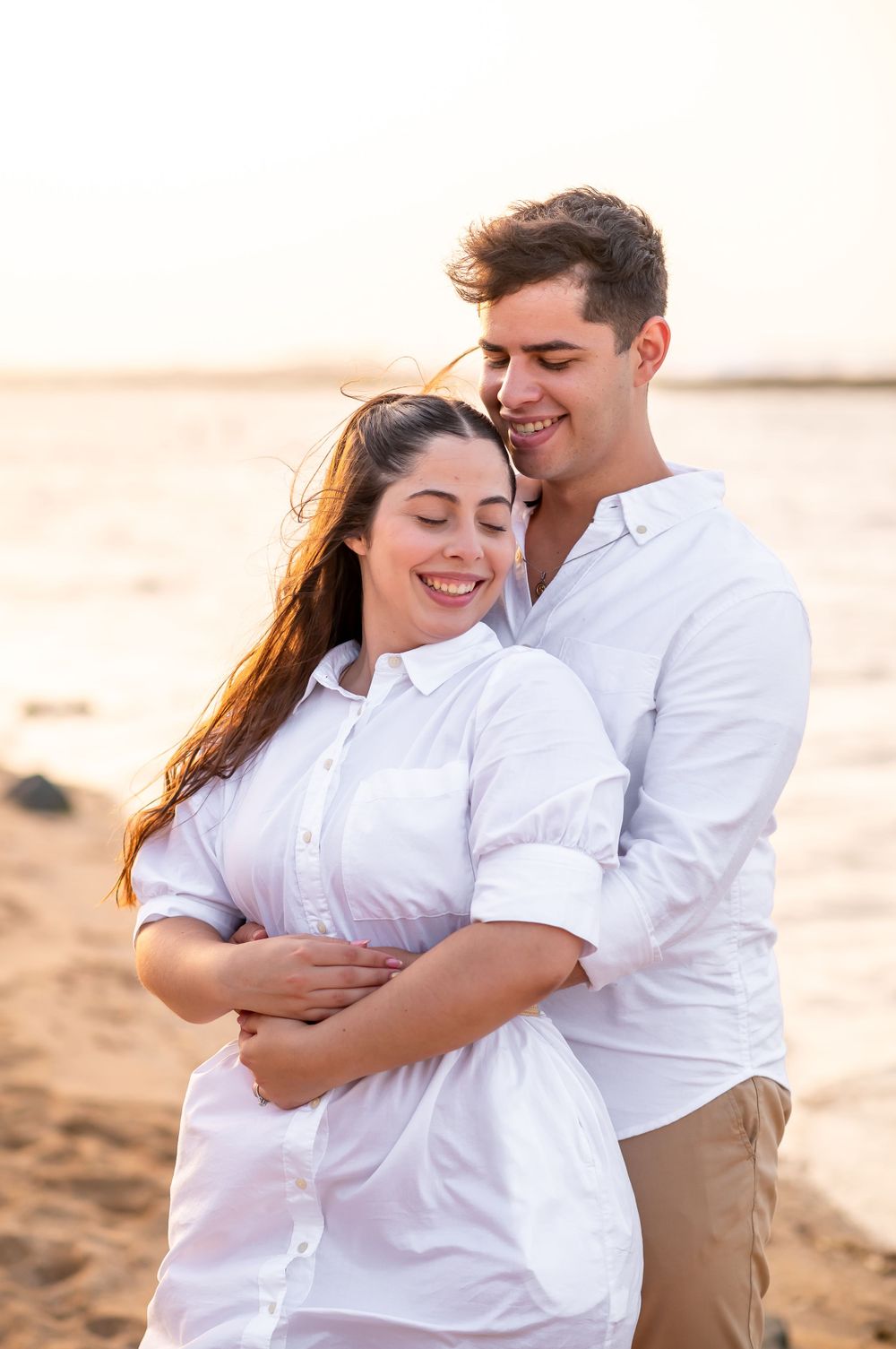 A tender embrace captured on a sunlit beach during golden hour.