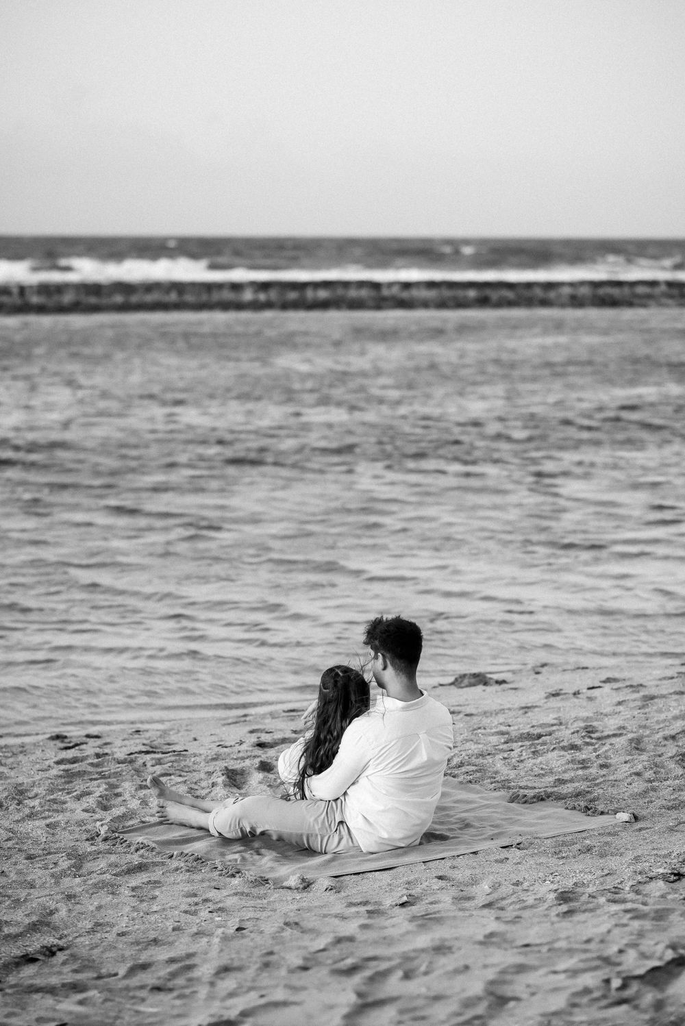 A couple sitting together on the beach watching the ocean waves.