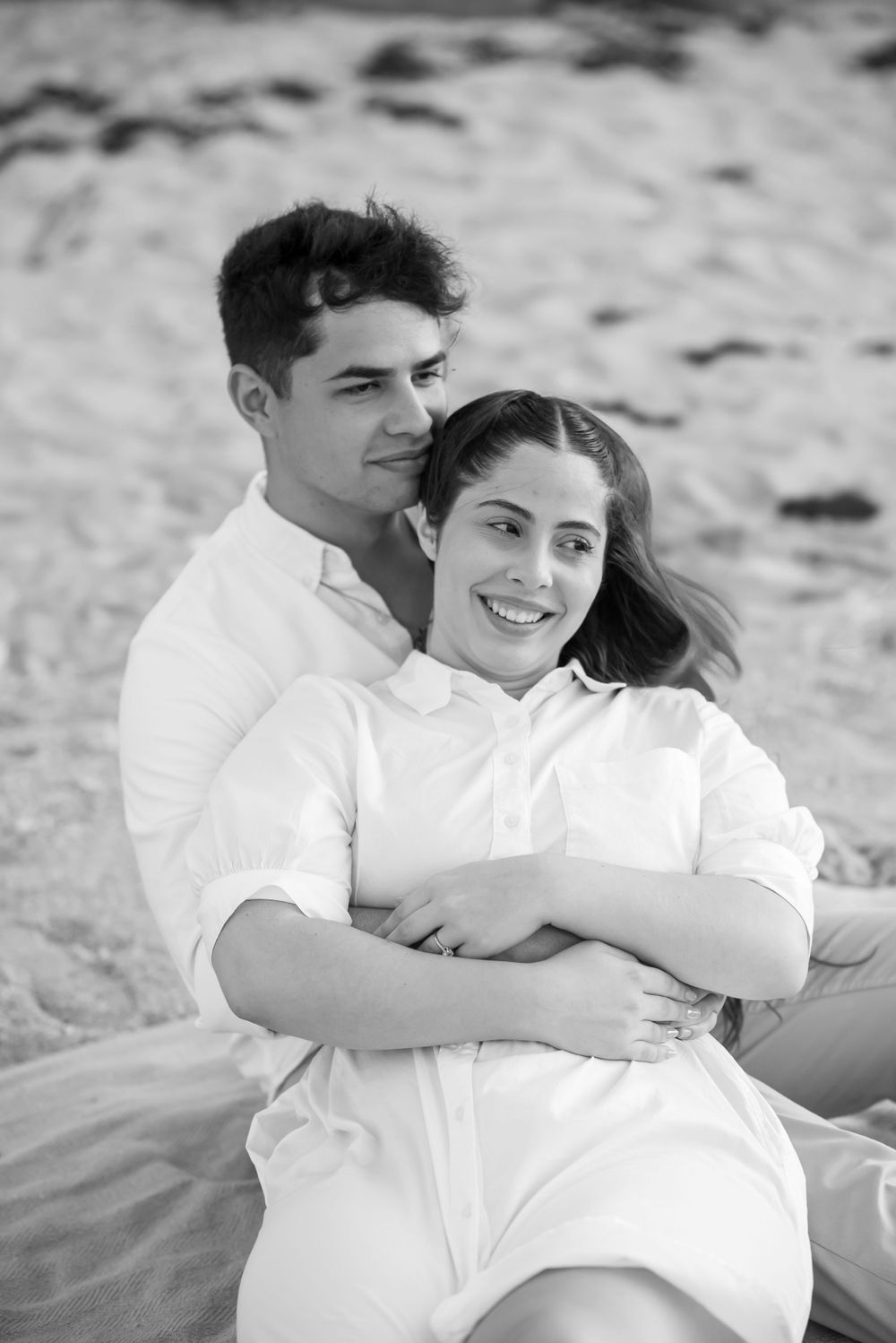 A loving couple in white clothing sharing an intimate moment on the beach.