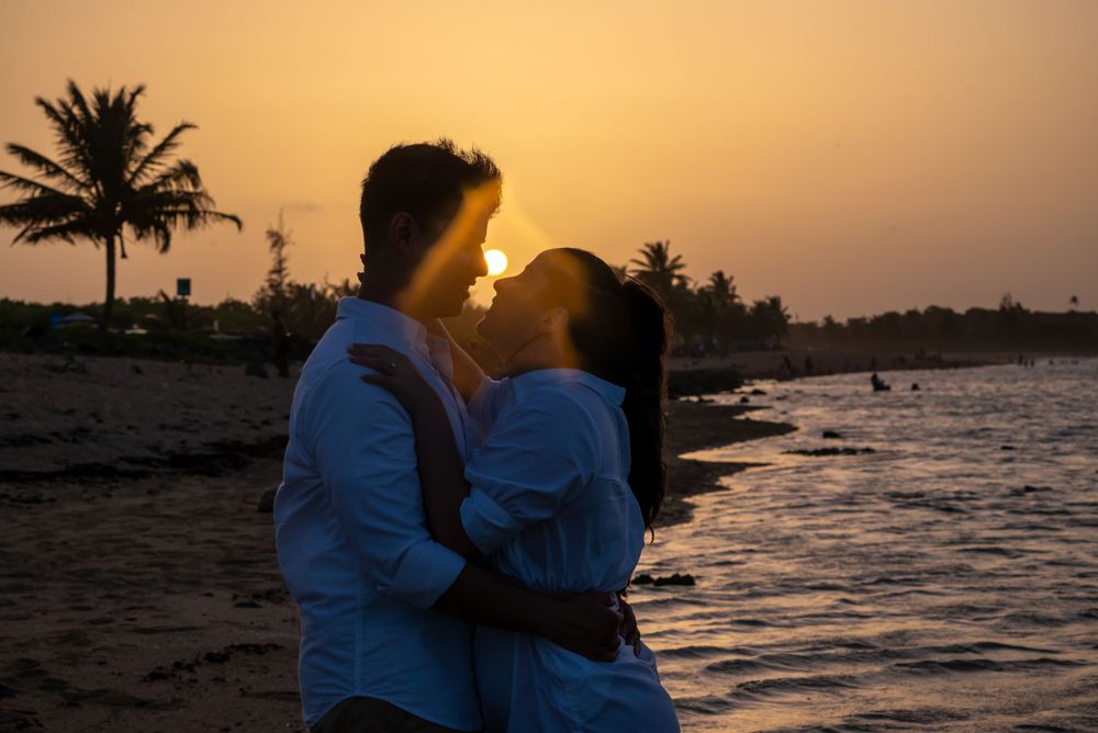A couple sharing a romantic moment at sunset with palm trees and ocean in the background.