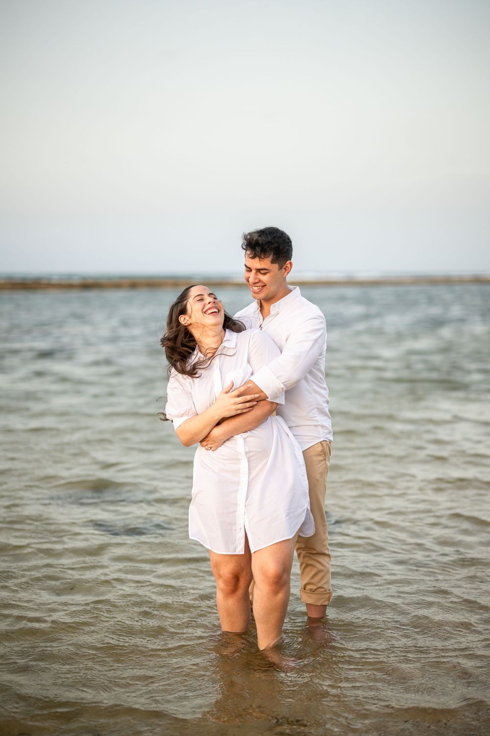 A couple laughing together while standing in shallow ocean water.