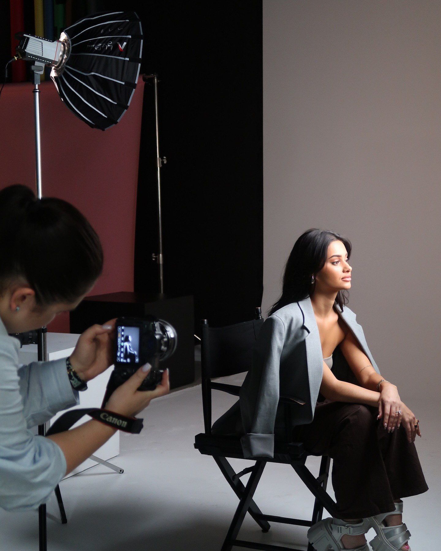Photographer capturing model during studio photoshoot with lighting equipment visible.