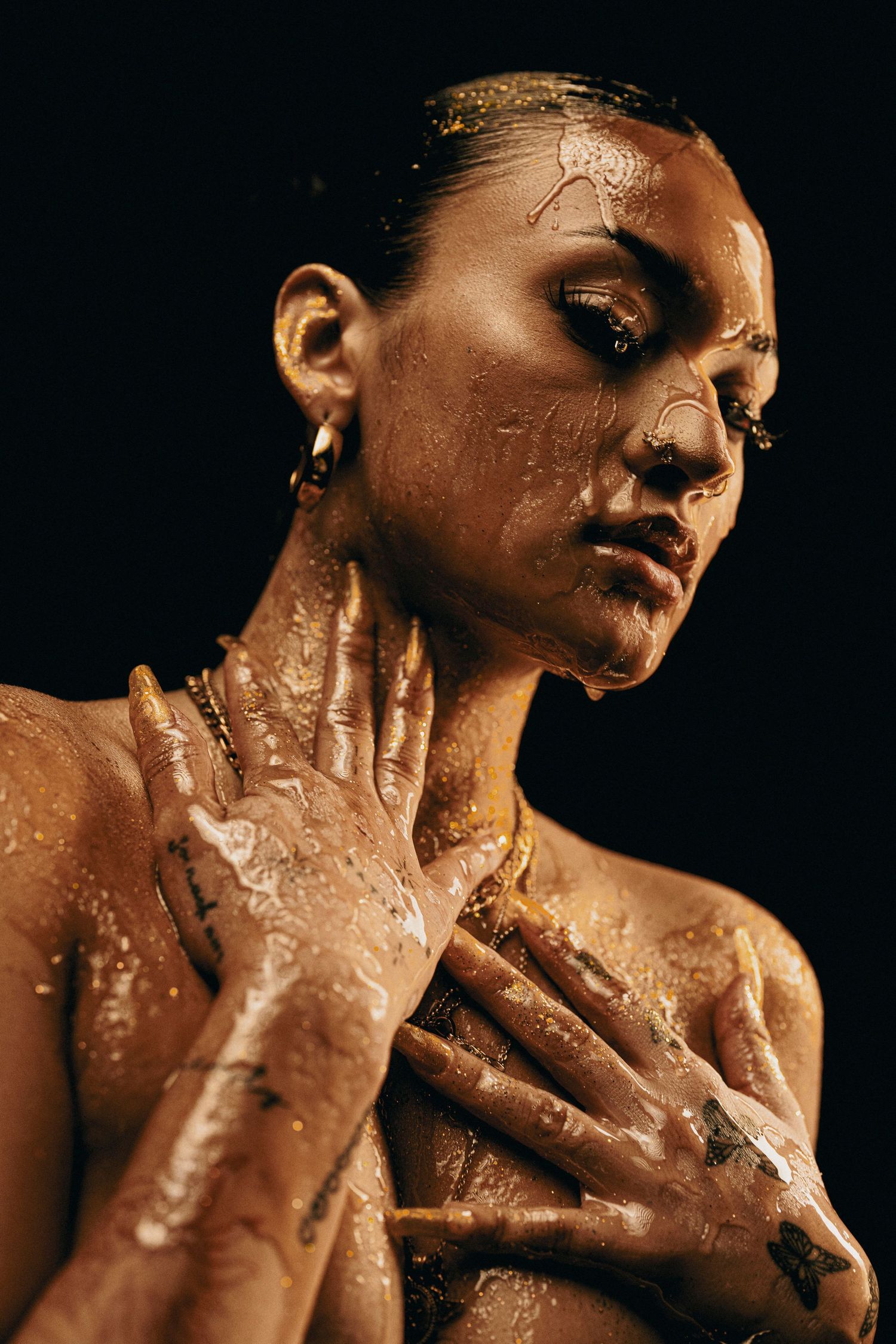 Artistic portrait with metallic gold body paint in dramatic lighting against dark background.