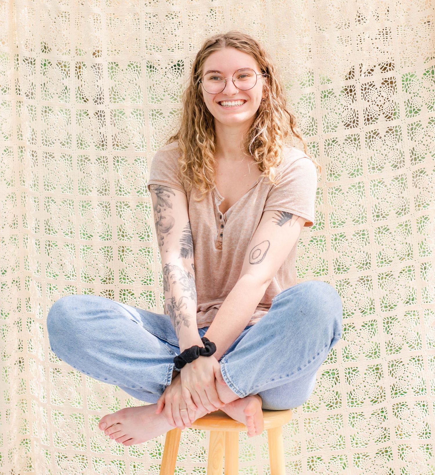 Lifestyle portrait scene with beige macrame backdrop and wooden chair in outdoor setting.