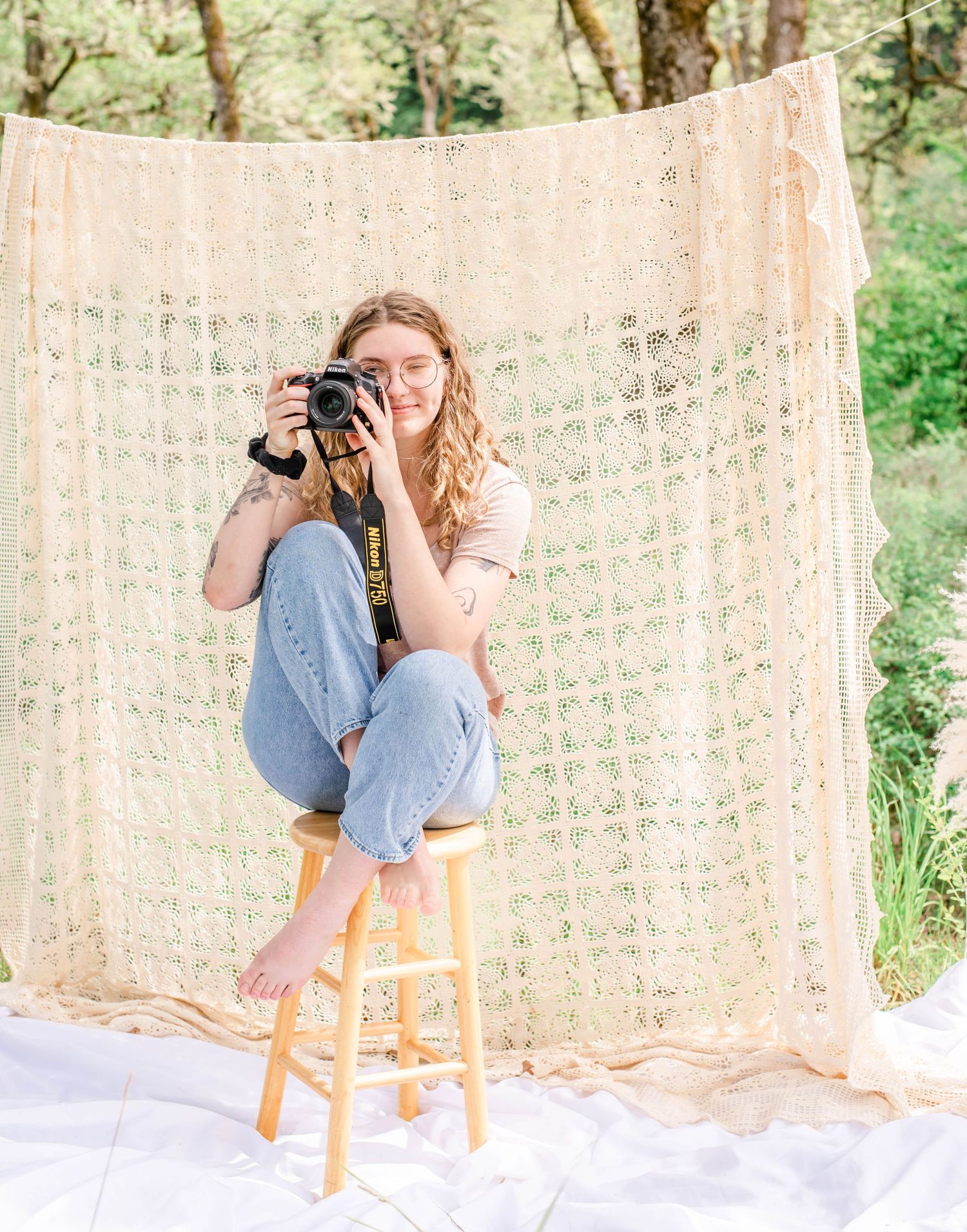 Artistic outdoor setup with delicate lace backdrop and wooden stool against forest greenery.
