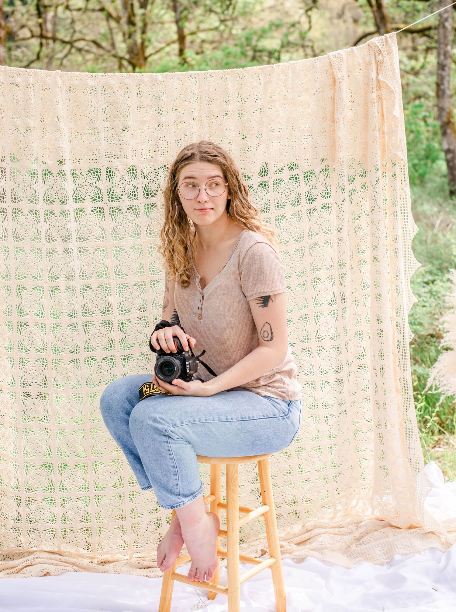 Artistic portrait shows photographer with camera against macrame wall in outdoor setting.