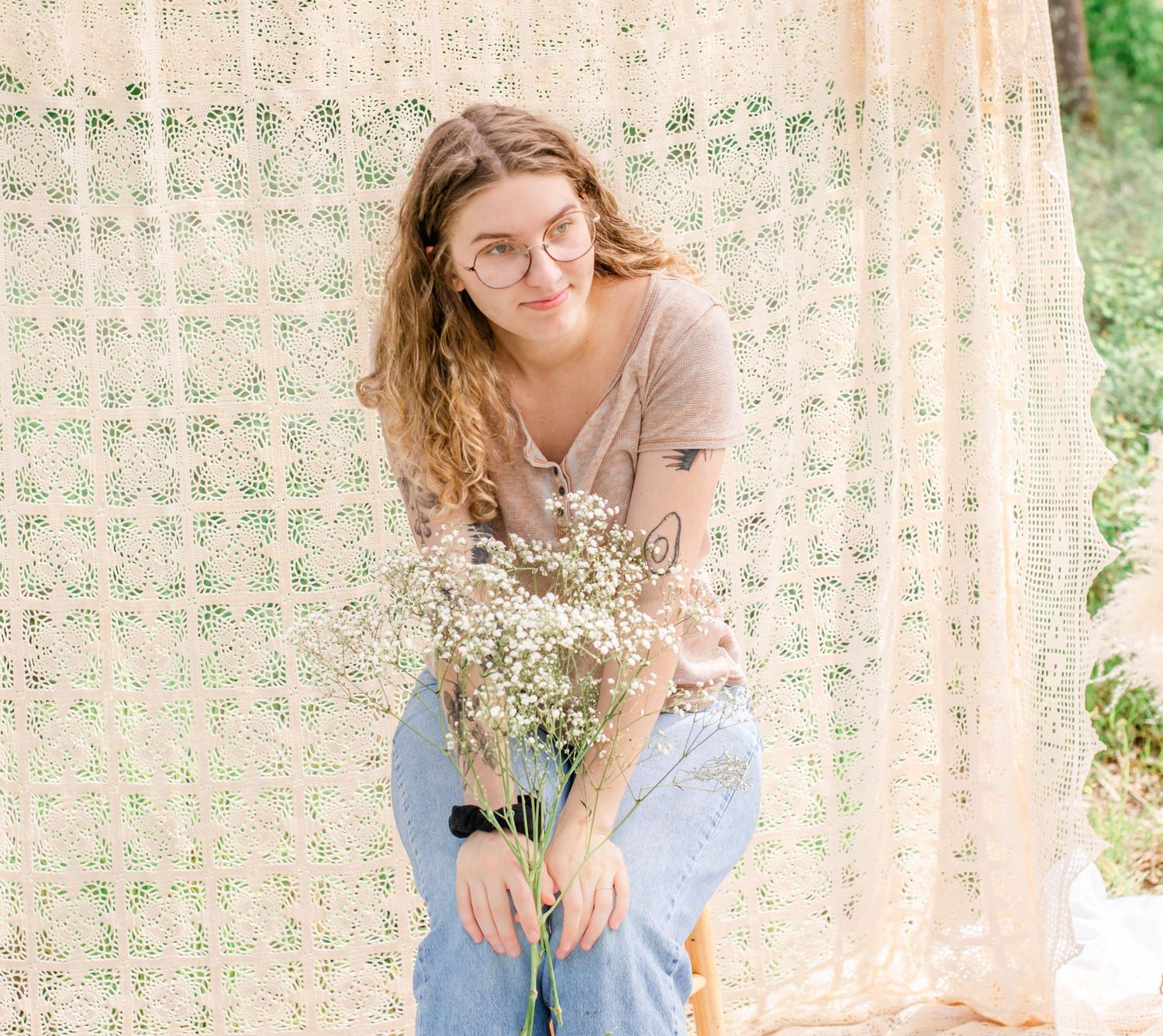 Woman in beige top poses against lace curtain backdrop with delicate baby's breath flowers.
