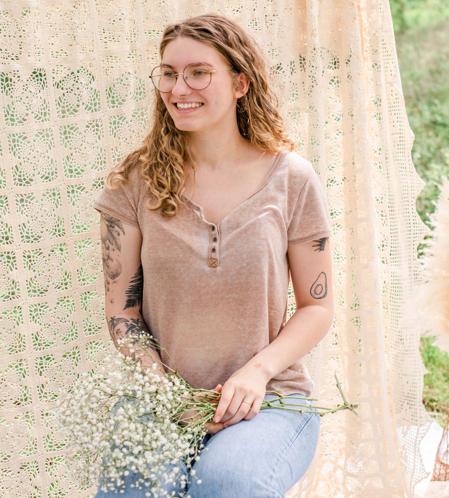 Woman in casual attire holds flowers while sitting against a floral lace backdrop.