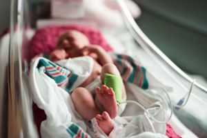 Hospital bassinet holds a sleeping newborn with colorful blankets.
