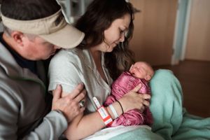 Parents lovingly embrace their newborn baby in hospital setting.