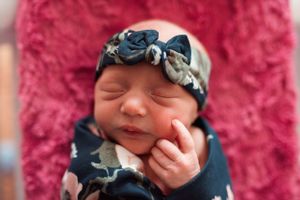 Newborn baby wearing a navy blue headband against a pink textured background.