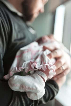 Gentle hands holding a white ruffled baby garment near a window.