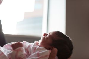Newborn baby in white sleeper resting peacefully in natural window light.