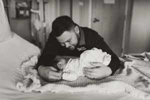 Intimate hospital room moment with newborn baby being cradled on blanket.