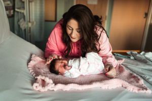 Mother in pink sweater lovingly gazing at newborn on hospital bed.