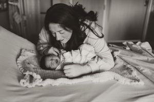 Black and white image showing intimate bonding moment with newborn on hospital bed.