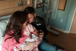 New parents sharing tender moment with their newborn in hospital room.