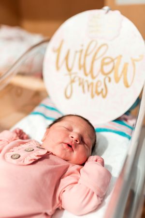 Newborn baby sleeping peacefully in a hospital bassinet with a decorative sign above.