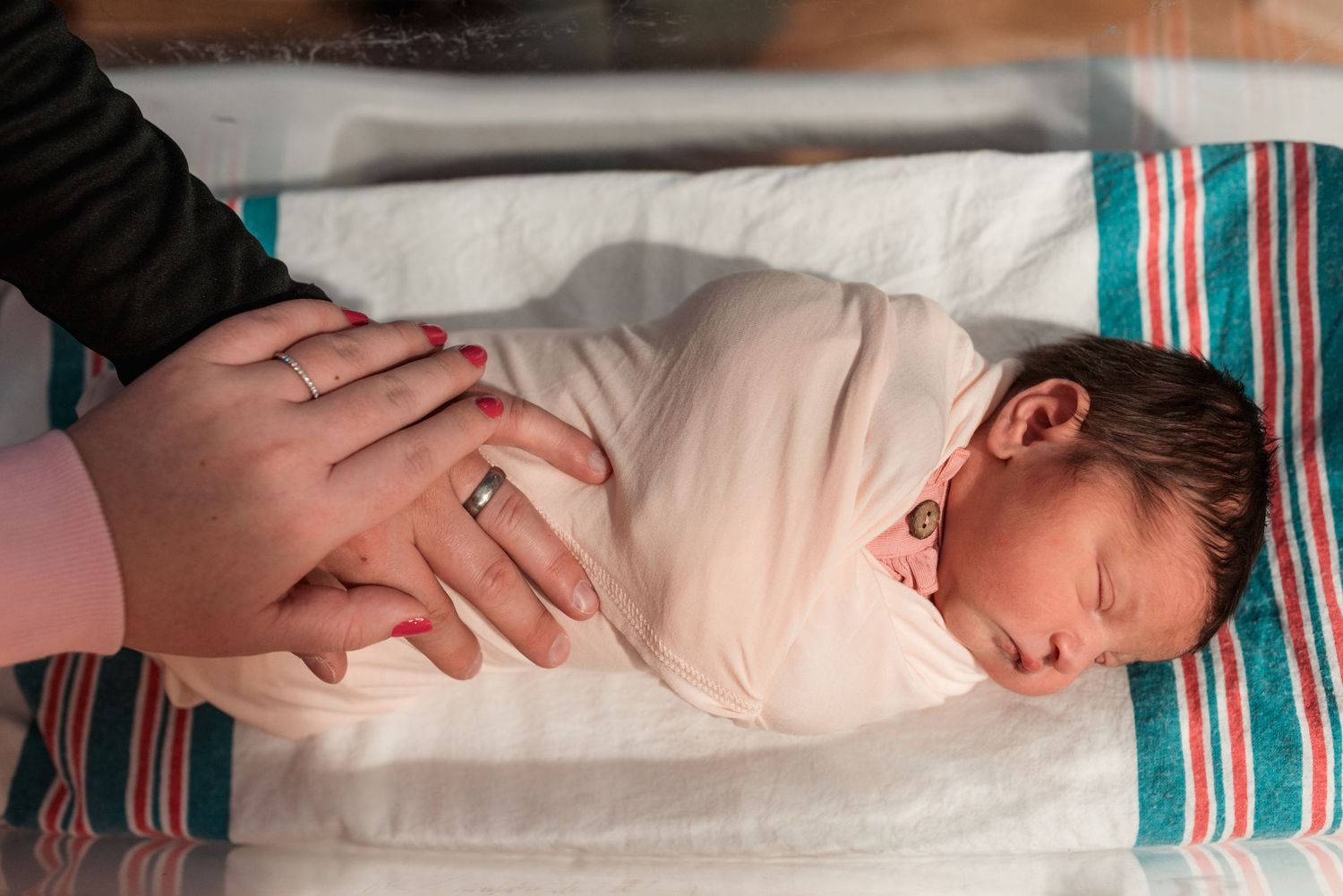Hospital staff checking on a swaddled newborn baby in a medical bassinet.