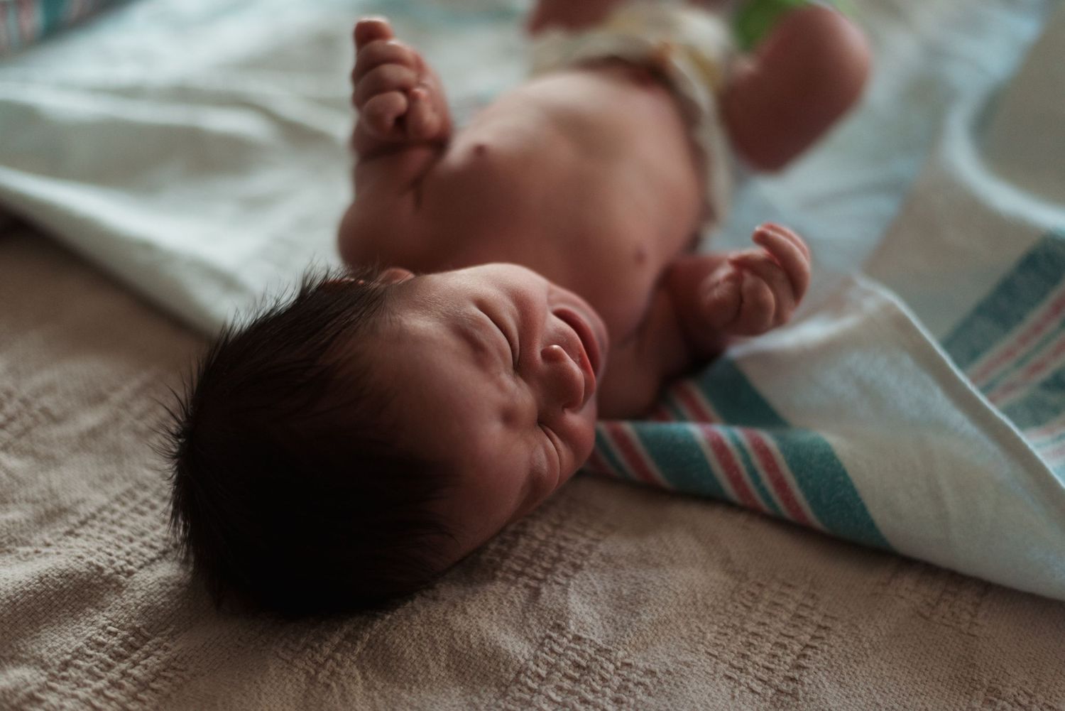 Peaceful sleeping newborn baby lying on patterned blanket in natural lighting.