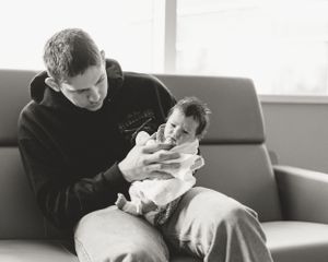 Adult feeding a small infant on a couch in black and white.