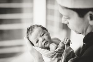 Parent gently cradling a sleeping newborn baby near a bright window.