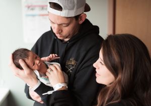 Parents sharing intimate moment with their newborn by window.