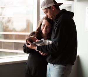 Intimate black and white portrait of parent holding their newborn baby by a window.