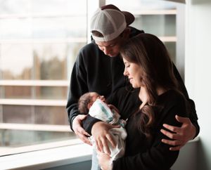 Family bonding moment with newborn baby near bright window.