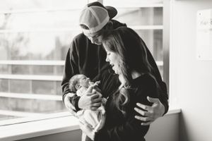 Parents sharing a special moment with their newborn baby in natural window light.