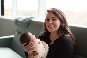 Candid lifestyle photo of parents with their newborn baby by a bright window.