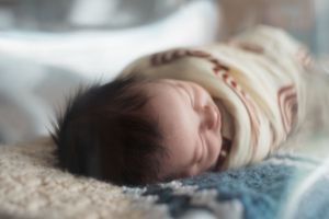 Peaceful sleeping newborn wrapped in soft blankets during lifestyle photoshoot.