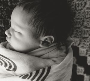 Close-up black and white portrait of a sleeping newborn baby in striped clothing.