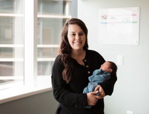 Parents holding newborn baby in bright white modern room.