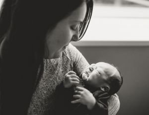 Parent in gray sweater cradling newborn baby during indoor photography session.