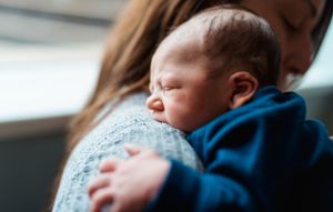 Newborn baby wearing blue outfit being held during Fresh 48 photography session.