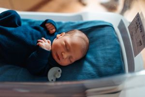Baby in blue outfit resting peacefully during indoor lifestyle photography.