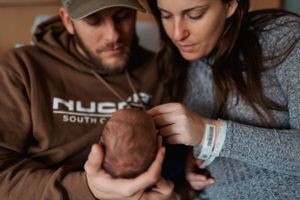 Parents tenderly holding and gazing at their newborn baby wrapped in a gray blanket.