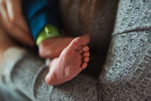 Delicate newborn baby feet resting on a textured gray blanket.