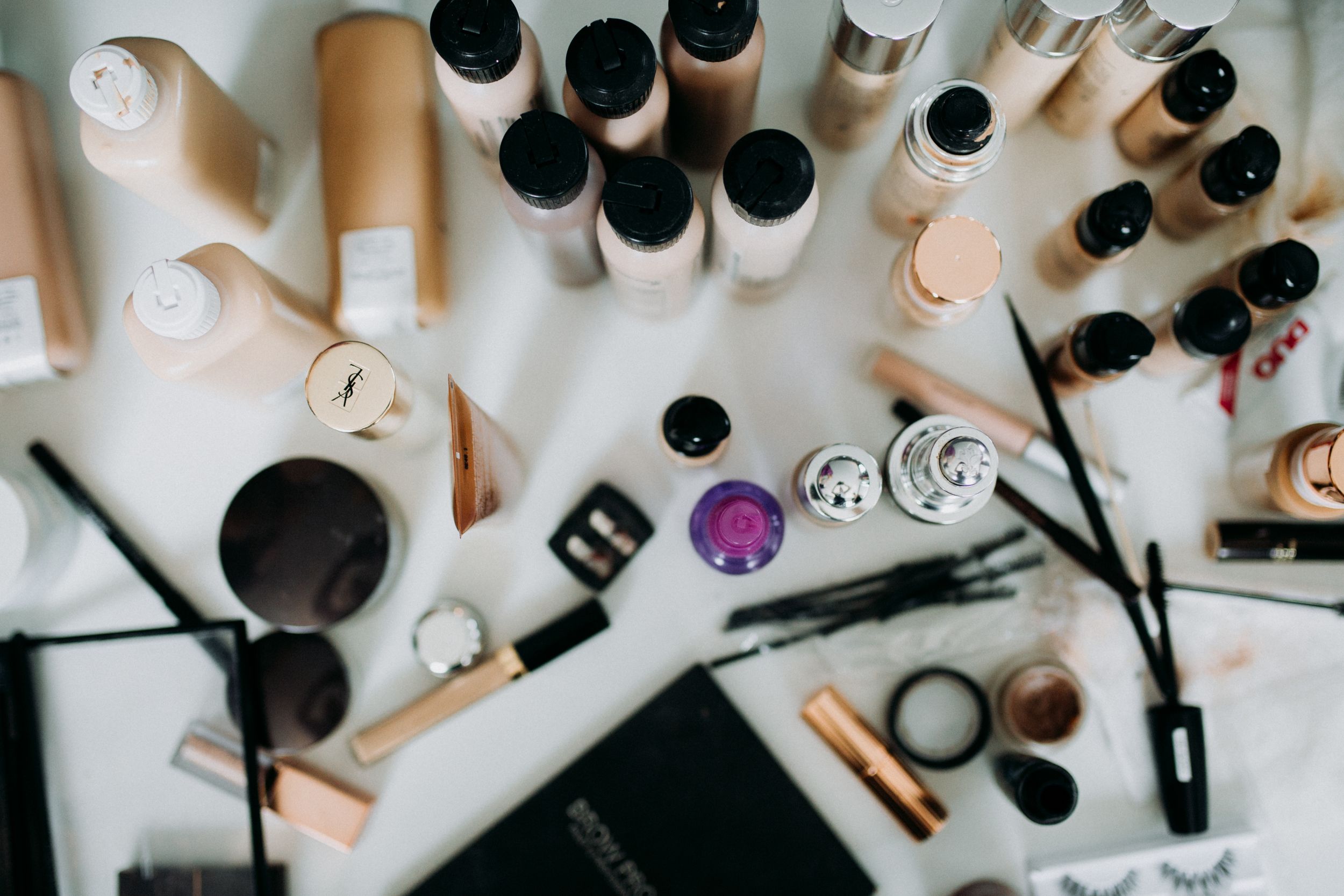Makeup products and brushes arranged on a white surface including bottles and applicators.