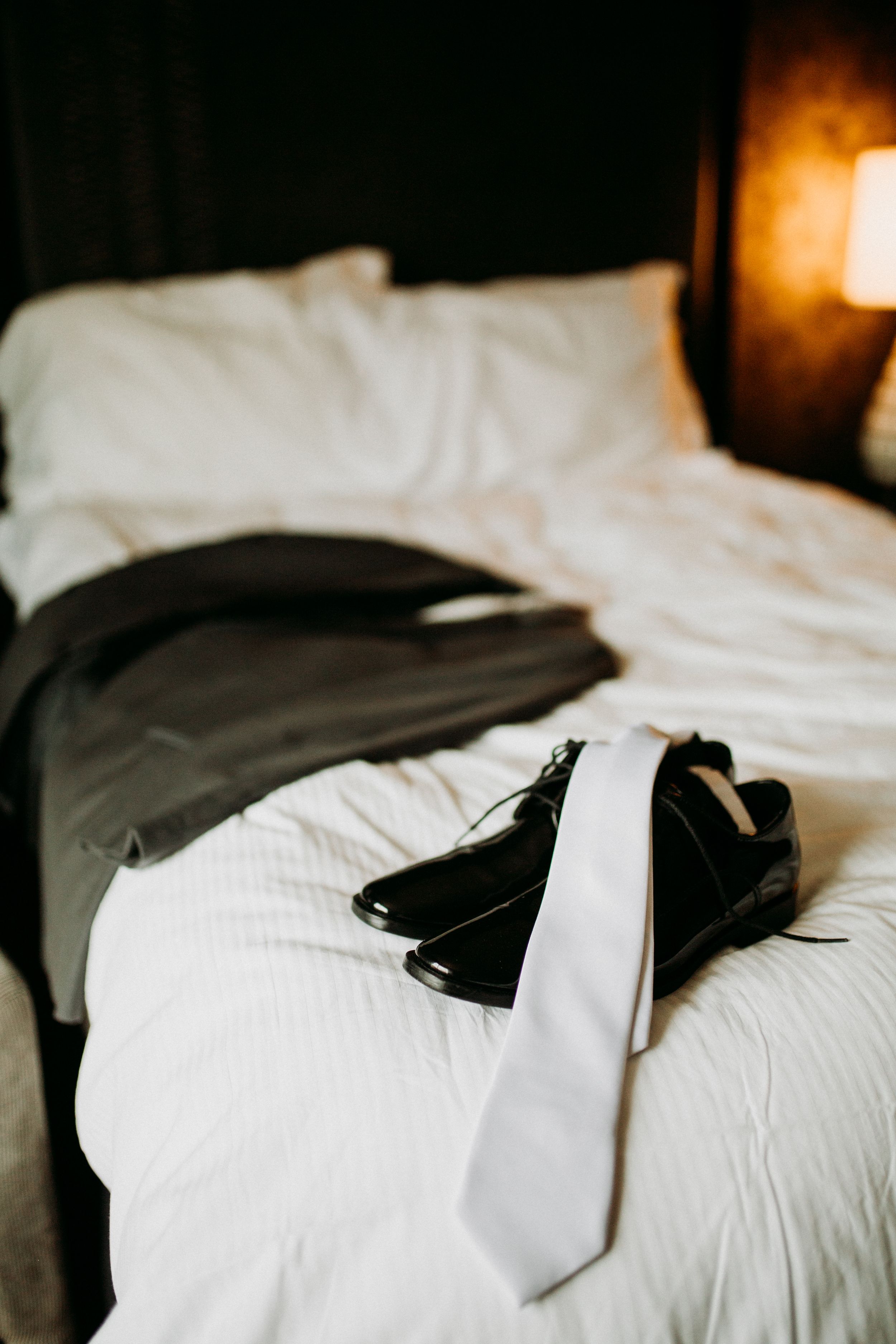 A white tie and black dress shoes arranged on a hotel bed.