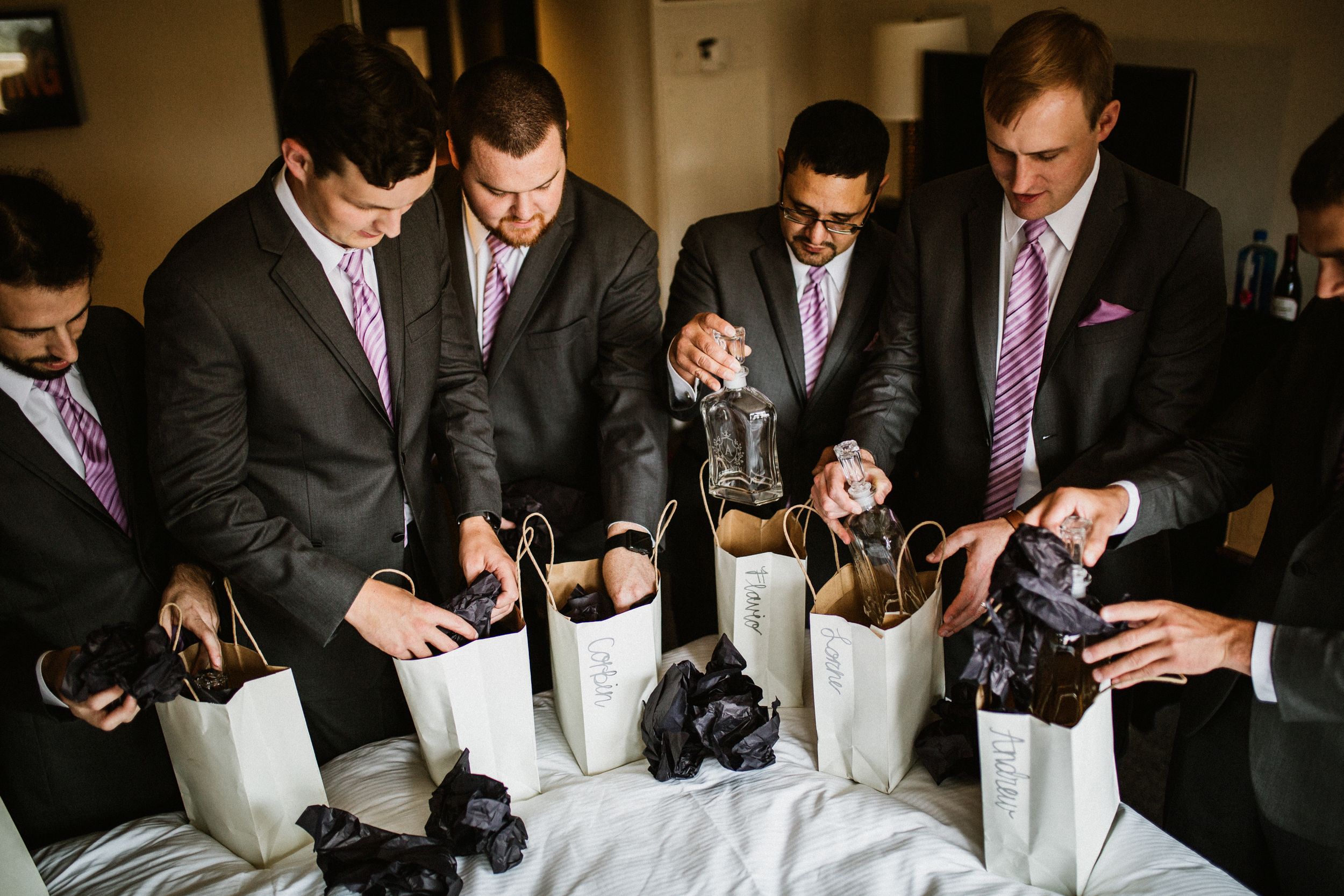 Groomsmen in suits examining contents of gift bags during wedding preparations.