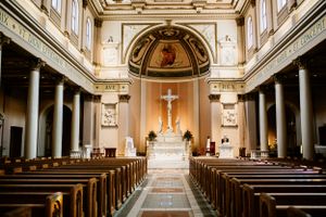 Ornate Catholic church interior with long aisle leading to illuminated altar and crucifix.
