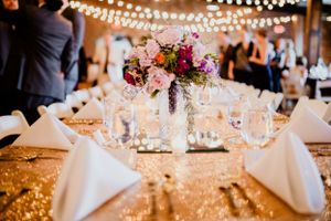 Elegant wedding reception table with pink floral centerpiece and string lights overhead.