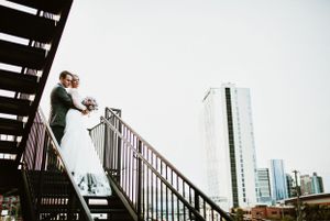 Urban wedding portrait on metal staircase with city skyline backdrop.