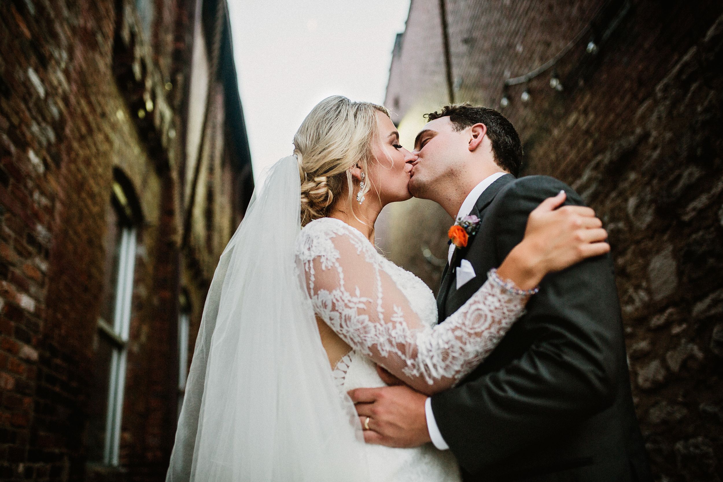 Intimate wedding kiss against rustic brick wall background.