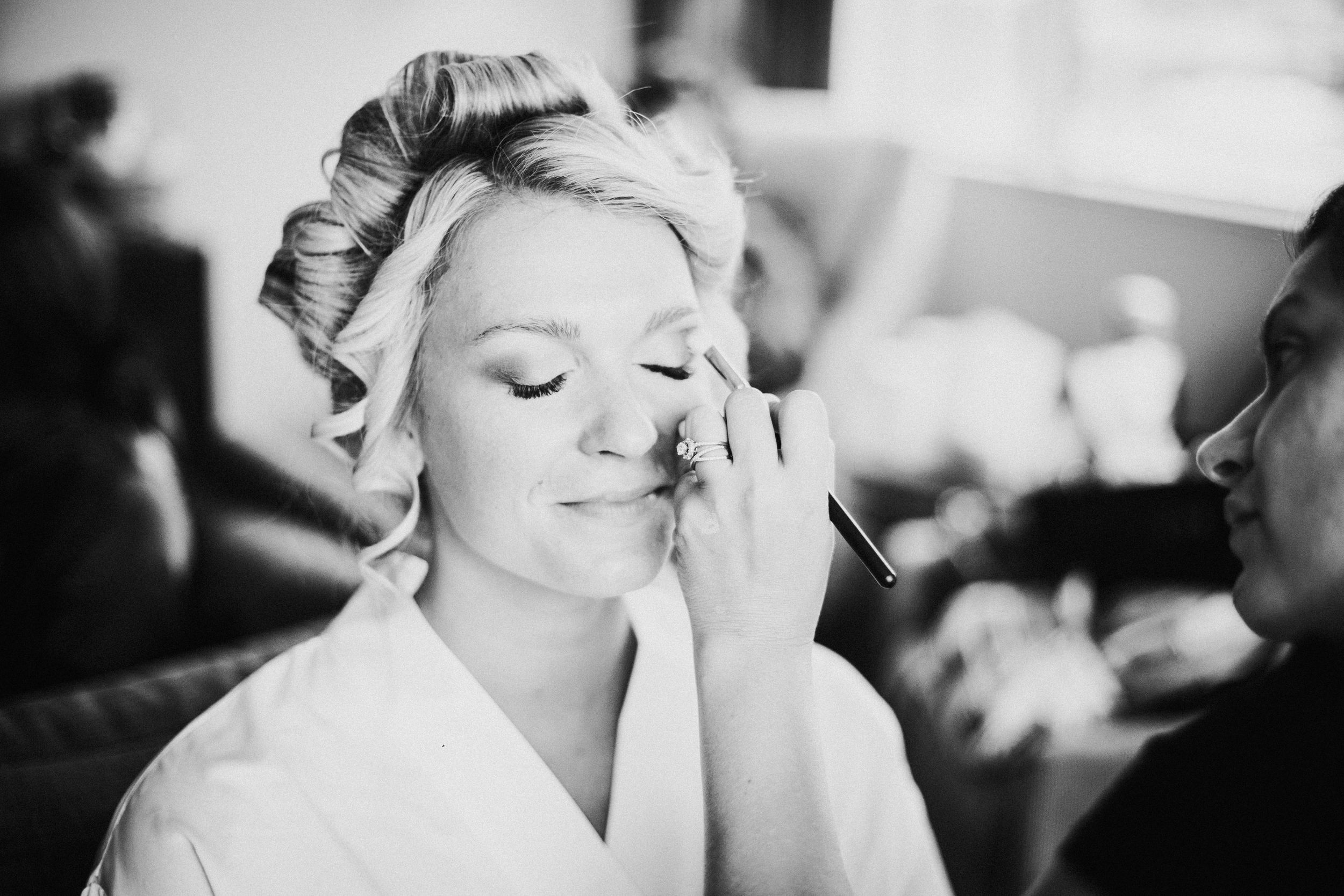 Black and white getting ready photo showing wedding day makeup application.