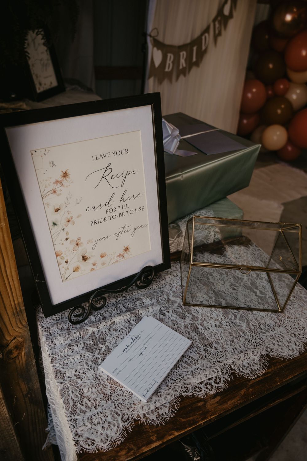 Elegant bridal shower recipe card display in black frame on lace-covered table with gift box.