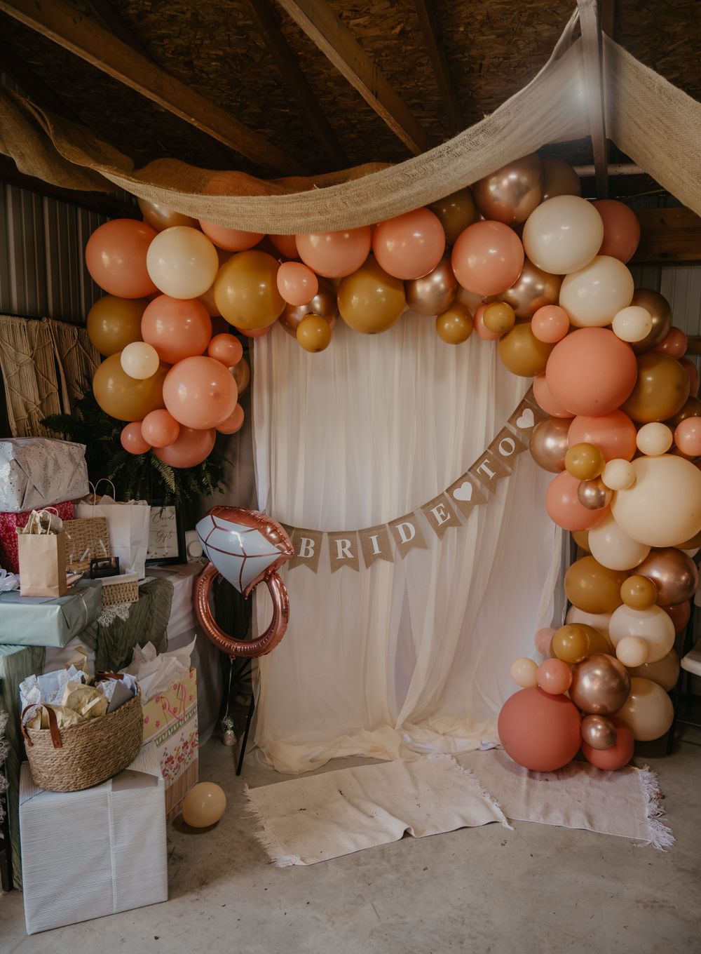 Boho bridal shower balloon arch in peach, gold, and cream with a Bride-to-Be banner and gift table.